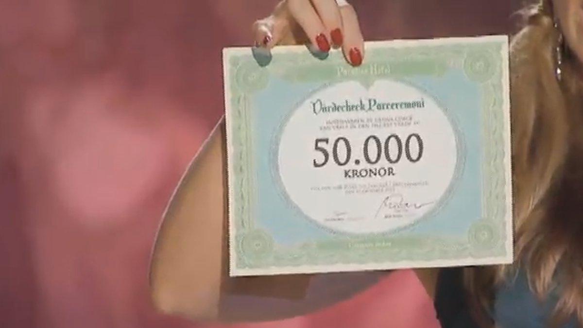 Programledare Malin Gramer sträcker fram en check på 50 000 kronor. 